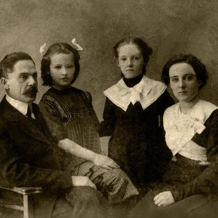 Vintage photo of calm mother and father sitting in studio with daughters in old fashioned clothes