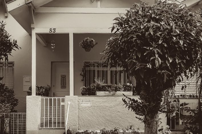 Early 1900s house with a gated porch; tree in front of the home.