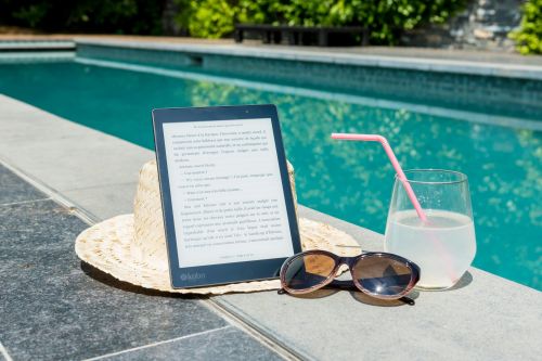 Sunny poolside scene with an e-reader, sunhat, sunglasses, and drink for ultimate relaxation.