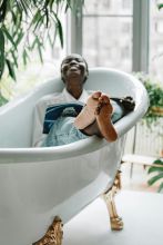 African American woman enjoying leisure time in a bathtub surrounded by greenery, creating a peaceful ambiance.