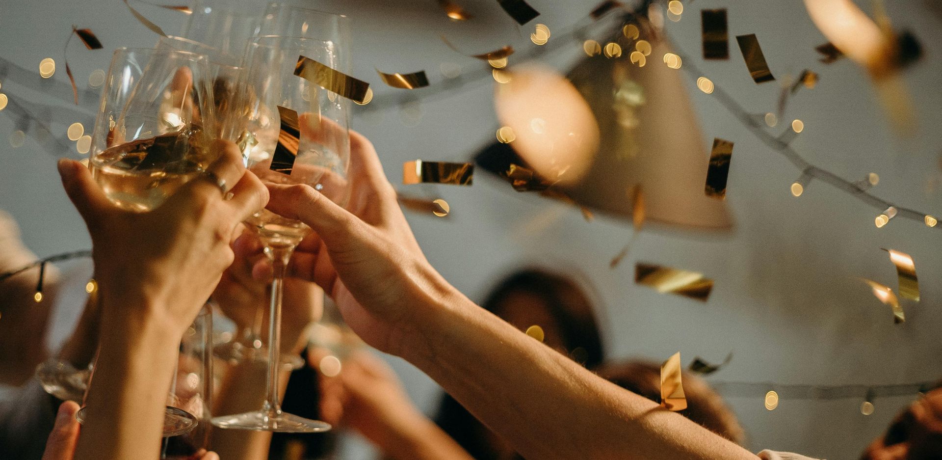 A lively indoor party scene with people toasting champagne glasses amid confetti and warm lights.