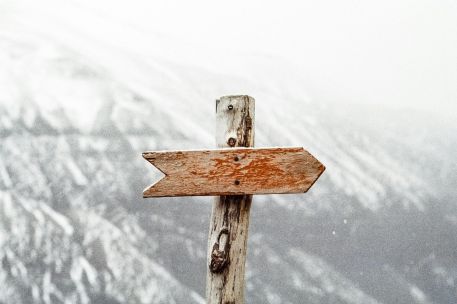 A wooden arrow signpost points the way amidst a snowy mountain landscape.