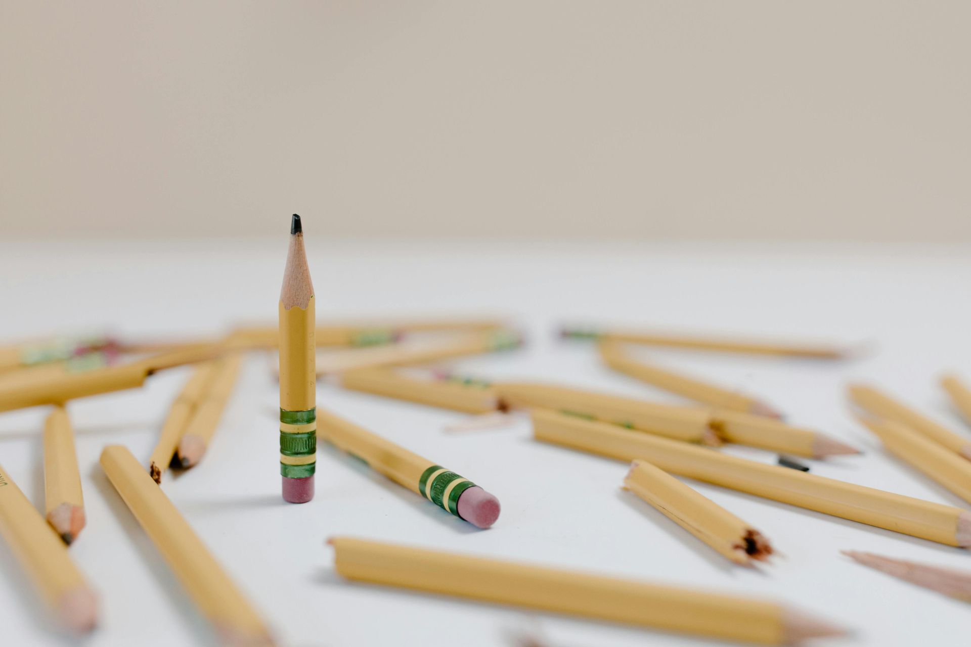 A single upright pencil stands among scattered pencils on a white surface.