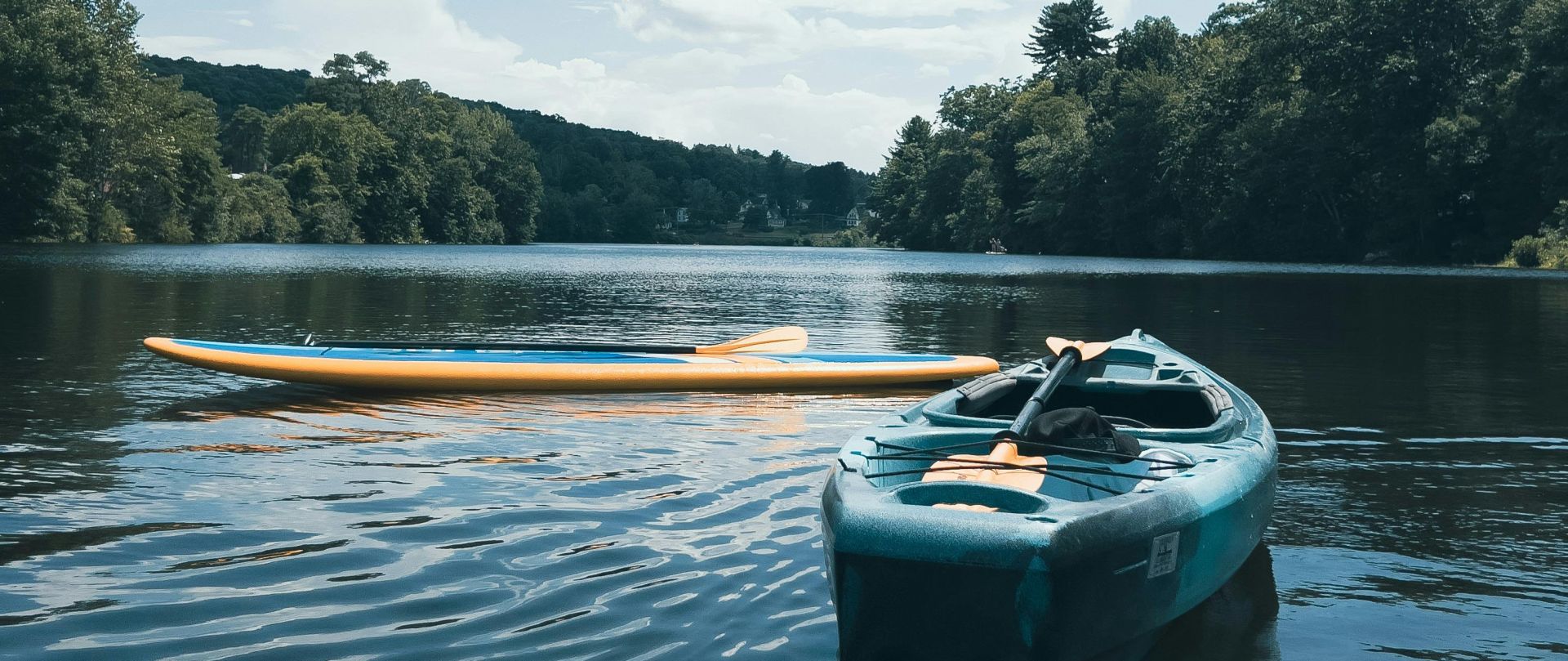Peaceful scenery of kayaks floating on a lake under a bright sky, surrounded by greenery.