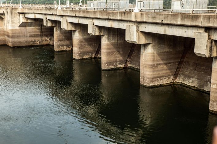 A robust concrete dam structure with reflections over a calm water surface.