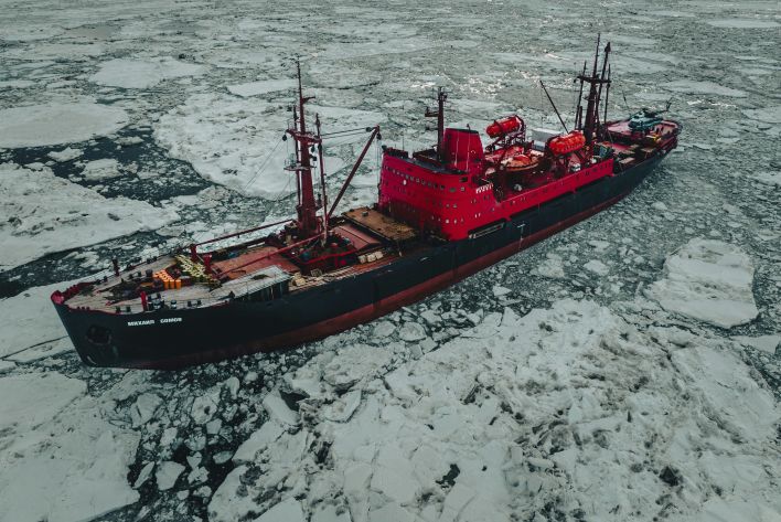 Aerial view of a red icebreaker ship navigating through the icy waters of the Russian Arctic.