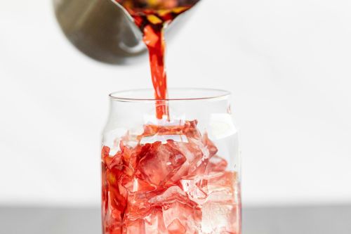 Refreshing hibiscus tea being poured over ice cubes in a clear glass, capturing a vibrant burst of color.