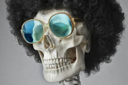 A skeleton wearing an afro wig and sunglasses, set against a gray background.