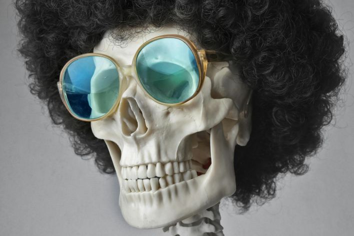A skeleton wearing an afro wig and sunglasses, set against a gray background.