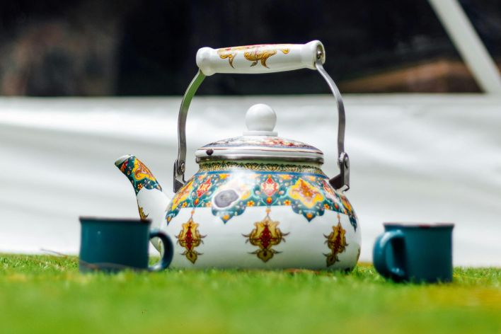 Colorful ornate teapot and cups on grass, perfect for a garden tea setting.