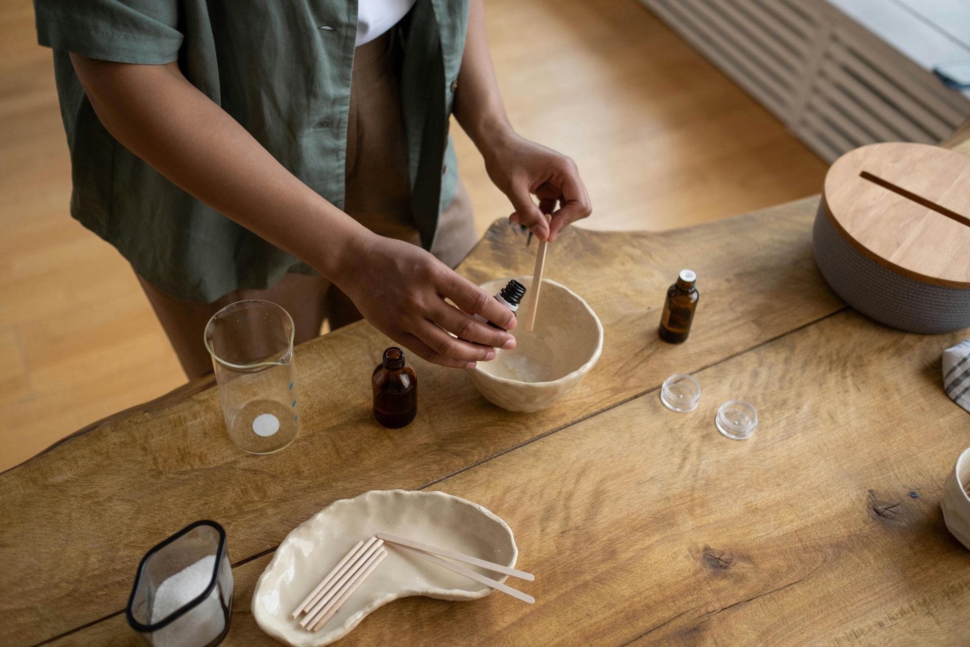 Close-up of hands making homemade lip balm in a cozy indoor setting.
