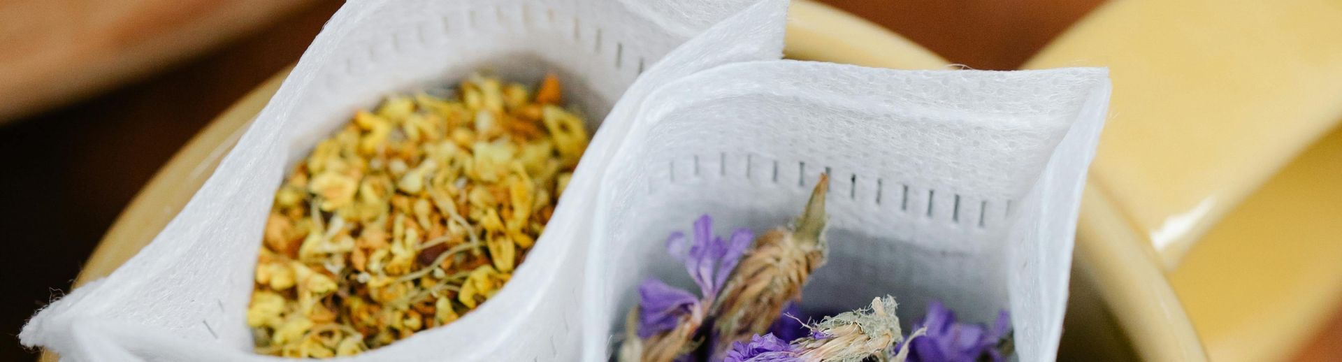Top view of various herbal teabags with flowers in a yellow mug on a wooden table.
