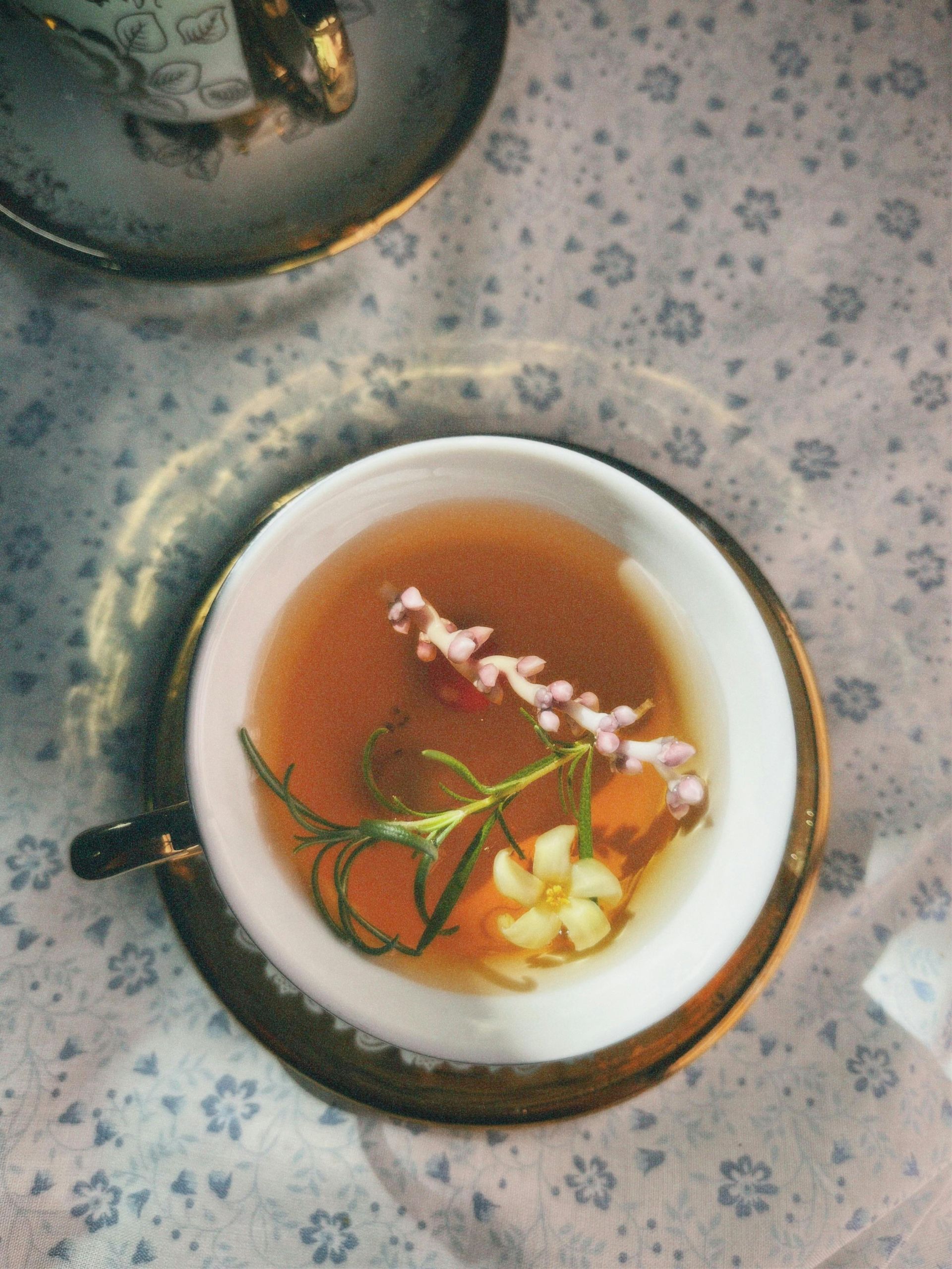 Overhead view of herbal tea in a floral cup with garnishes, set on a patterned tablecloth.
